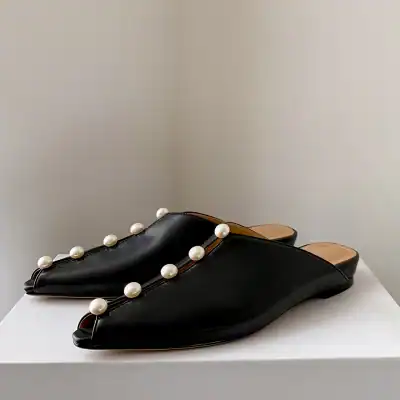 Stylish black leather slip-on mules decorated with elegant white pearls, perfect for a sophisticated look. Ideal for casual or formal occasions, combining comfort and luxury.