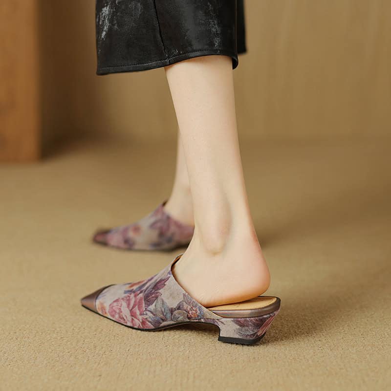 Delicate floral-patterned slip-on slippers with a pointed toe and low heel, perfect for stylish indoor or outdoor wear, combining comfort and fashion.