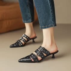 Close-up of trendy black women’s heels featuring multiple silver buckles and pointed toes, paired with rolled denim jeans, perfect for fashionable and comfortable footwear.