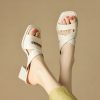 Close-up of stylish white sandals with crisscross straps on a woman's feet, showcasing comfortable and trendy footwear suitable for casual or dressy occasions.