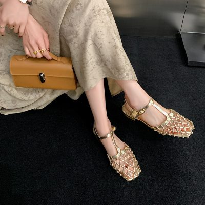 Fashionable gold sandals with intricate netted straps and ankle buckles, perfect for chic occasions, paired with a beige floral dress and matching accessories.