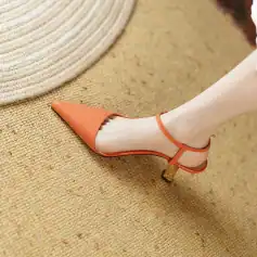 Close-up of a stylish orange high heel with ankle strap on a textured beige surface, emphasizing fashionable footwear and trendy shoe styles for women.