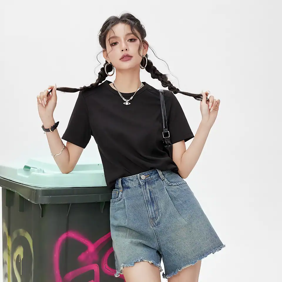 Young woman in a black t-shirt and denim shorts, posing casually with playful braid styles and fun accessories, in bright minimal setting, showcasing trendy streetwear fashion.
