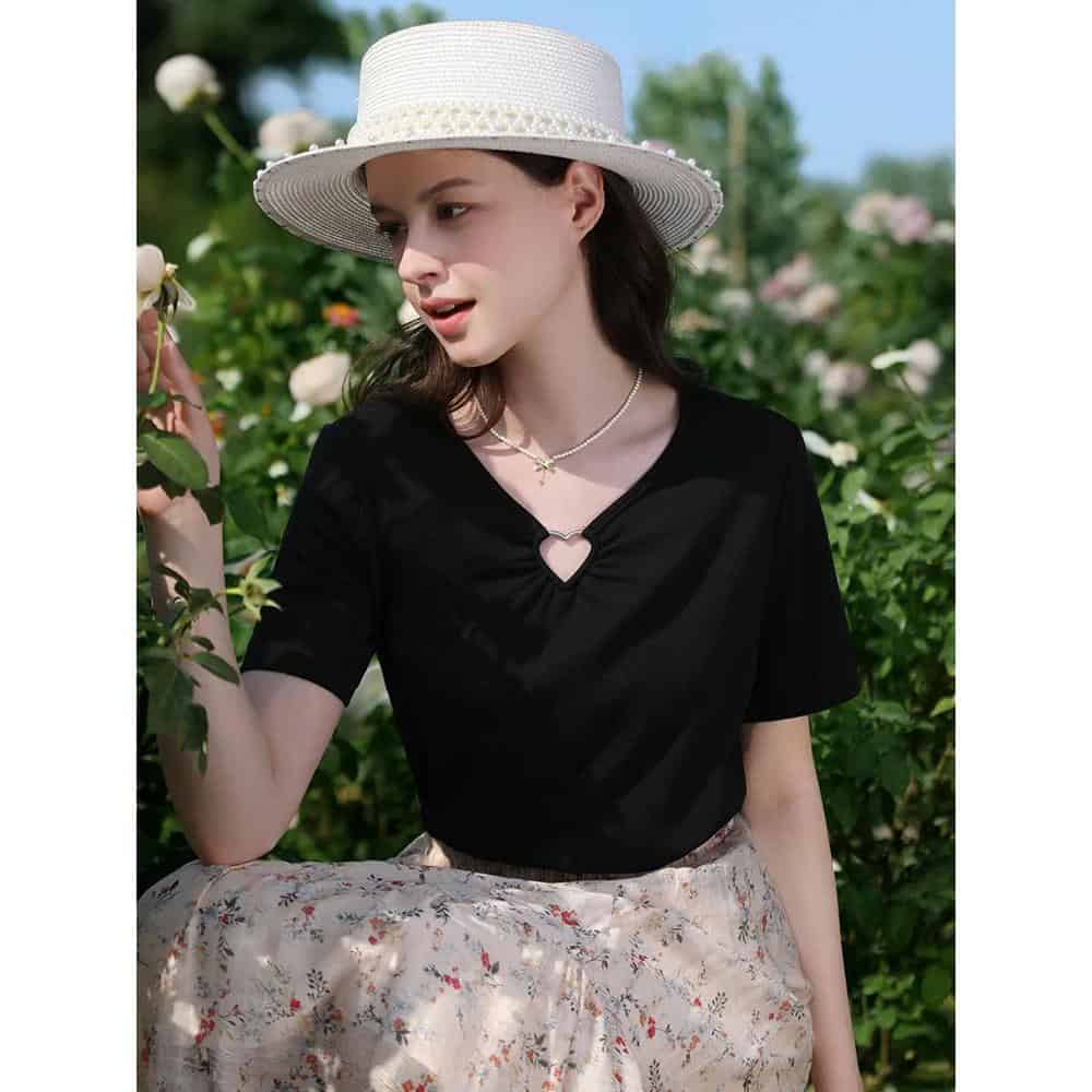 A stylish young woman wearing a black top and a wide-brimmed white hat, enjoying a garden setting, showcasing fashionable accessories perfect for optometry and eyewear shopping at Monalisa Store.