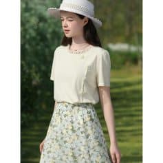 A stylish woman wears a soft beige summer dress with floral patterns, accessorized with a white sun hat, perfect for outdoor casual wear or shopping at Monalisa Store.