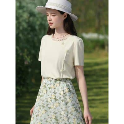 A stylish woman wears a soft beige summer dress with floral patterns, accessorized with a white sun hat, perfect for outdoor casual wear or shopping at Monalisa Store.