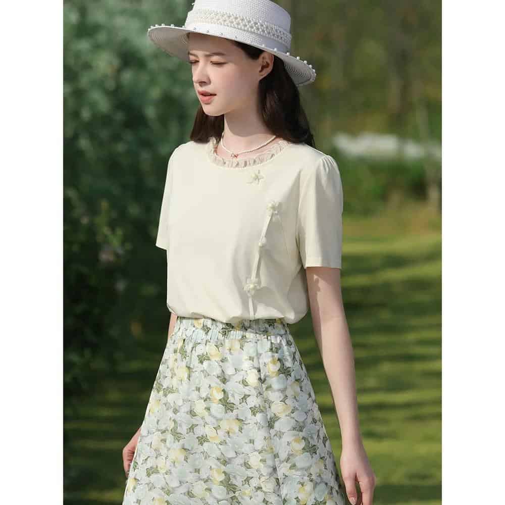 A stylish woman wears a soft beige summer dress with floral patterns, accessorized with a white sun hat, perfect for outdoor casual wear or shopping at Monalisa Store.