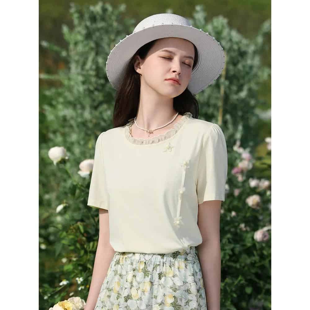 Young woman wearing a stylish white hat, light yellow top, and floral skirt in a garden setting, perfect for summer fashion, outdoor wear, and spring style inspiration.