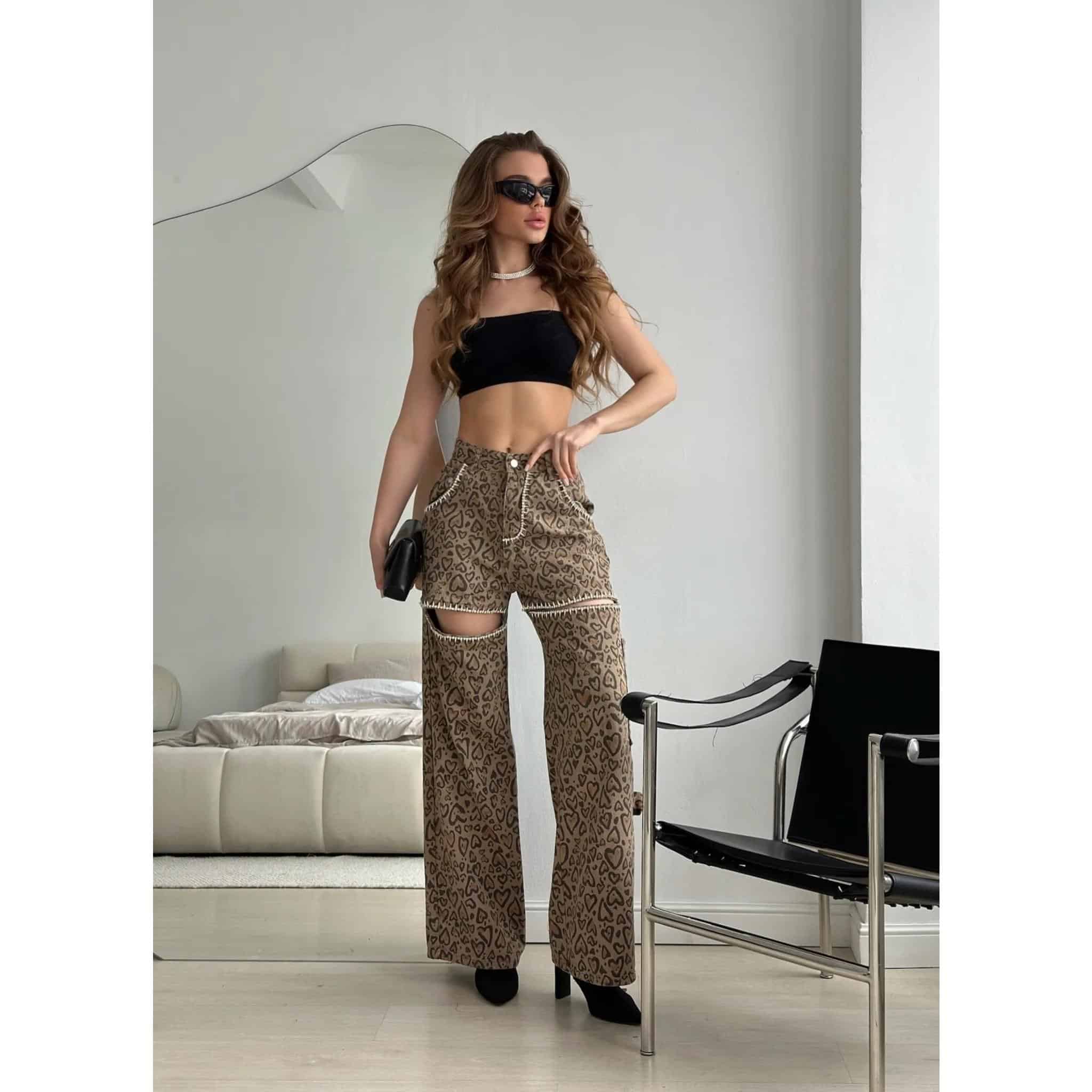 Stylish woman wearing trendy sports bra and leopard print wide-leg pants with cutouts, accessorized with sunglasses, necklace, and clutch bag, showcasing modern fashion.