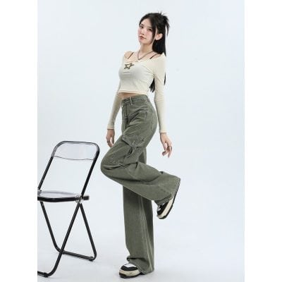 Young woman in trendy casual outfit with wide-leg cargo pants and a crop top, posing confidently with a chair in a minimalist studio setting.