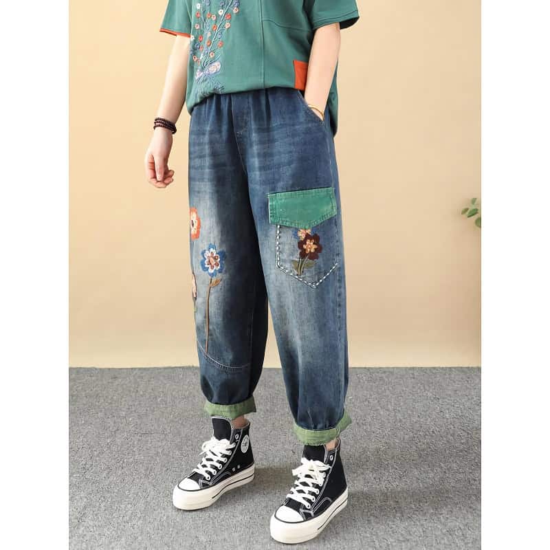 Stylish denim jeans featuring floral embroidery, a colorful patch pocket, and rolled cuffs, perfect for casual fashion and streetwear.