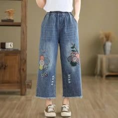 Comfortable denim jeans with colorful tennis-inspired embroidery, club logos, and distressed details, perfect for trendy casual wear in a modern fashion store.