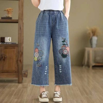 Comfortable denim jeans with colorful tennis-inspired embroidery, club logos, and distressed details, perfect for trendy casual wear in a modern fashion store.