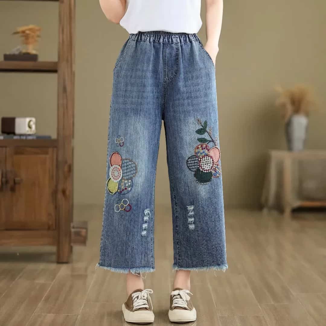 Comfortable denim jeans with colorful tennis-inspired embroidery, club logos, and distressed details, perfect for trendy casual wear in a modern fashion store.
