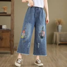 Comfortable denim wide-leg jeans with colorful floral embroidery and distressed details, perfect for casual fashion.