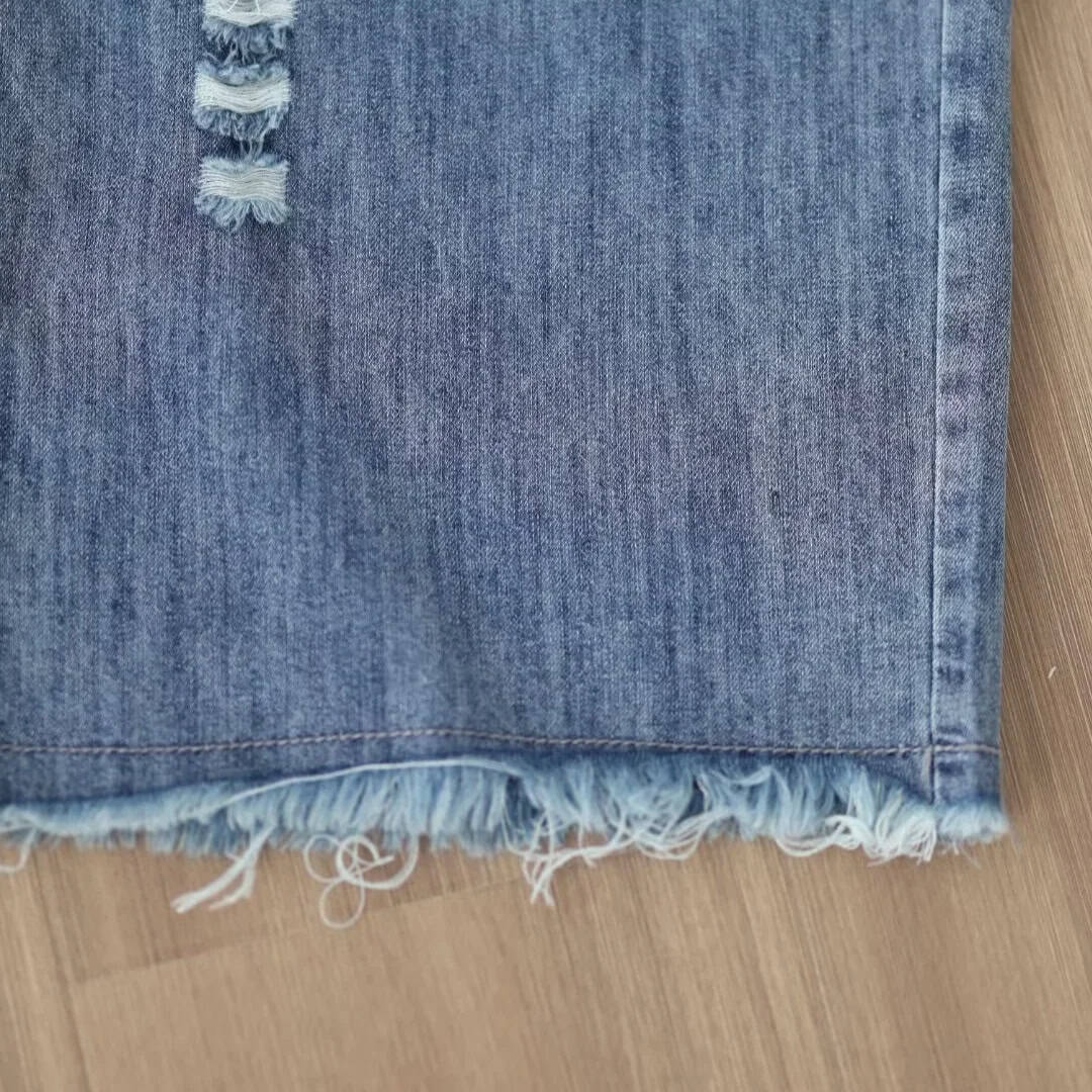Close-up of blue denim fabric with frayed hem, showcasing trendy distressed jeans for casual wear. Perfect for stylish, comfortable fashion enthusiasts.