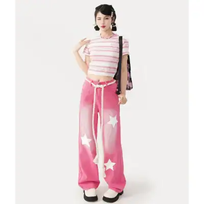 A stylish young woman in pink star print wide-leg pants and a striped crop top, carrying a backpack. Modern fashion look perfect for casual outings and fashion-forward street style.