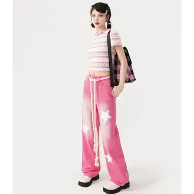Young woman wearing trendy casual outfit with pink tie-dye pants with stars, striped crop top, and stylish accessories, showcasing modern streetwear.