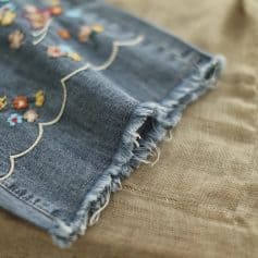 Brightly embroidered denim fabric featuring detailed floral design, ideal for stylish apparel and accessories, with frayed edges for a trendy, authentic look.