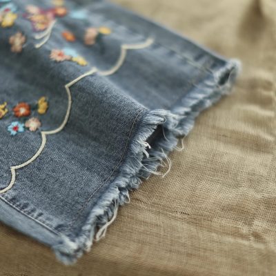 Brightly embroidered denim fabric featuring detailed floral design, ideal for stylish apparel and accessories, with frayed edges for a trendy, authentic look.
