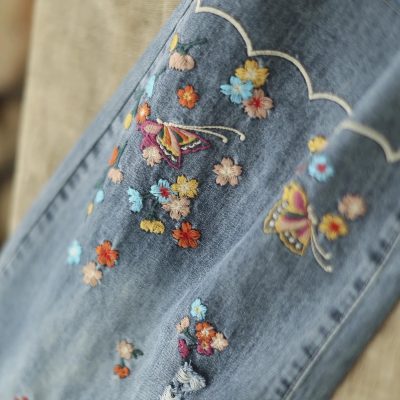 Denim jeans with intricate floral embroidery and butterfly designs, showcasing stylish and detailed fashion accessories perfect for modern casual wear.