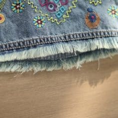 Close-up of colorful embroidered design on denim fabric showing detailed stitching and frayed edges. Perfect for customizing jeans or clothing accessories.