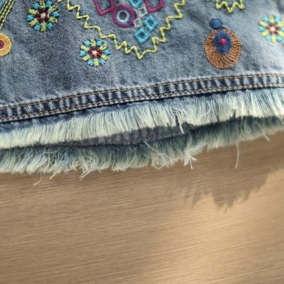 Close-up of colorful embroidered design on denim fabric showing detailed stitching and frayed edges. Perfect for customizing jeans or clothing accessories.