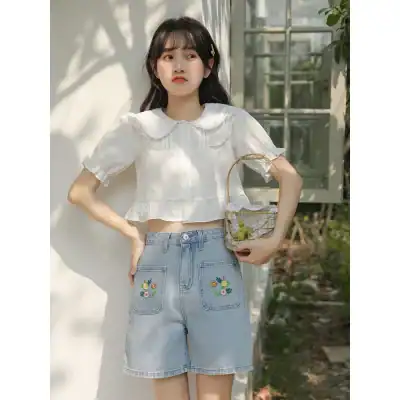 Girl in light denim shorts with floral embroidery, white blouse, and accessories at Monalisa Store, showcasing trendy apparel and eye care products.