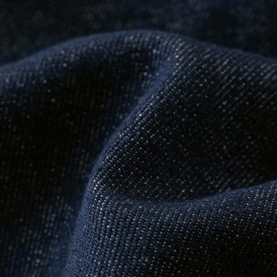 Close-up of dark blue denim fabric showcasing detailed stitching and texture, ideal for stylish clothing and accessories.