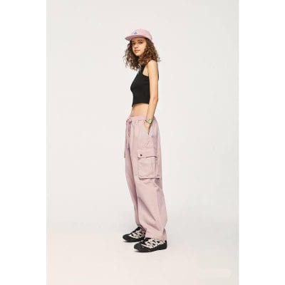 Young girl wearing trendy casual outfit with pink cargo pants, black sleeveless top, pink cap, and sporty sneakers, showcasing fashionable kids' clothing options.