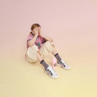 Young girl covering her face, sitting with sports drink, expressing stress or fatigue, positive environment, kid-friendly wellness products for children.