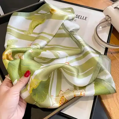 Luxurious silk scarf featuring a vibrant floral pattern in green, yellow, and white tones, perfect for adding sophistication to any outfit.