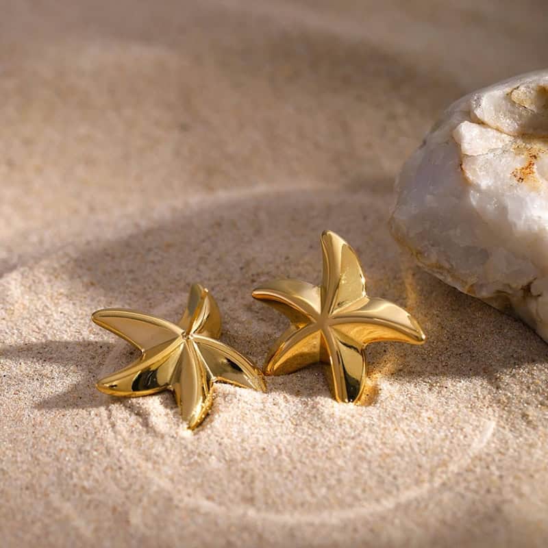 Elegant gold leaf earrings showcased on sandy beach with natural sunlight, highlighting luxurious jewelry suitable for fashion and special occasions.