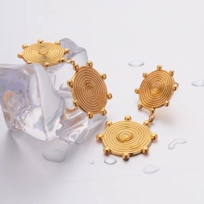 Elegant gold spiral earrings on clear ice sculpture with water droplets, luxury jewelry presentation, stylish accessories, Monalisa Medical store, fashion jewelry, sophisticated design.