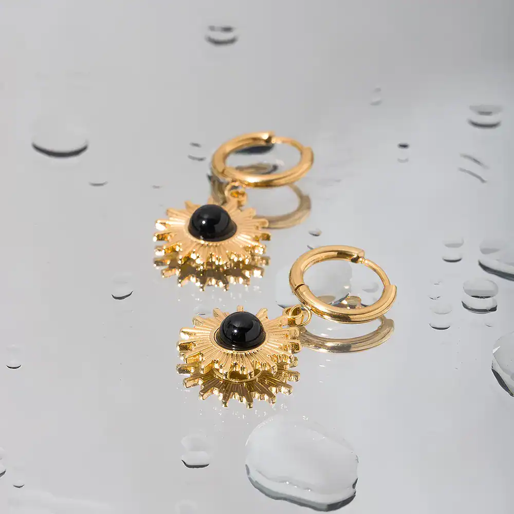 Golden hoop earrings featuring a sunray-inspired design with a black gemstone centerpiece, crafted for a sophisticated look. These jewelry pieces add a touch of luxury and elegance.