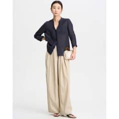 Stylish woman in a navy blouse and cream wide-leg trousers, holding a beige clutch, showcasing contemporary fashion and accessories from Monalisa Medical Store for a modern, sophisticated look.