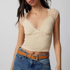 Elegant cream lace women's top with a V neckline, delicate cap sleeves, and a decorative bow detail for fashion-forward casual wear.