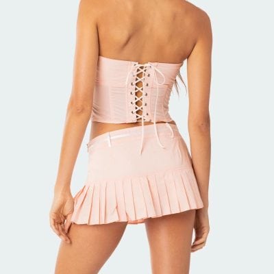 Fashionable pink corset with lace-up detail paired with a matching pleated mini skirt, perfect for trendy, chic looks and streetwear styles.