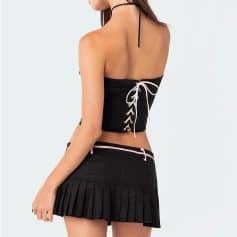 Close-up of a woman's back in stylish black crop top with lace-up detail and matching black pleated tennis skirt at Monalisa store, emphasizing trendy eyewear fashion and accessories.