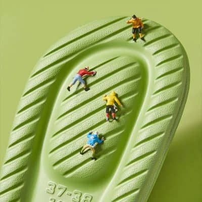Miniature figures climbing a textured green lens surface, emphasizing vision correction, eyewear, and optometry services.