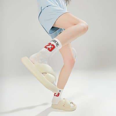 Cream-colored slides with trendy socks featuring a sports theme, showcasing casual yet fashionable footwear for everyday wear, ideal for a modern, youthful look.