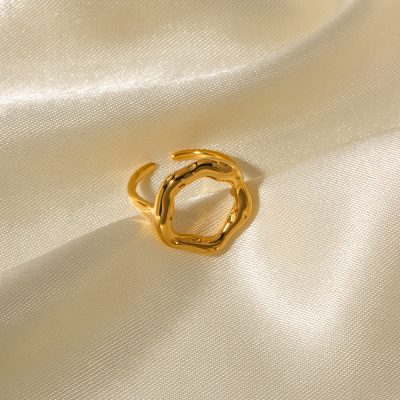 Alt text: Close-up of a stylish gold ring with an organic, irregular shape, placed on a silky, cream-colored fabric background, highlighting fine jewelry craftsmanship.