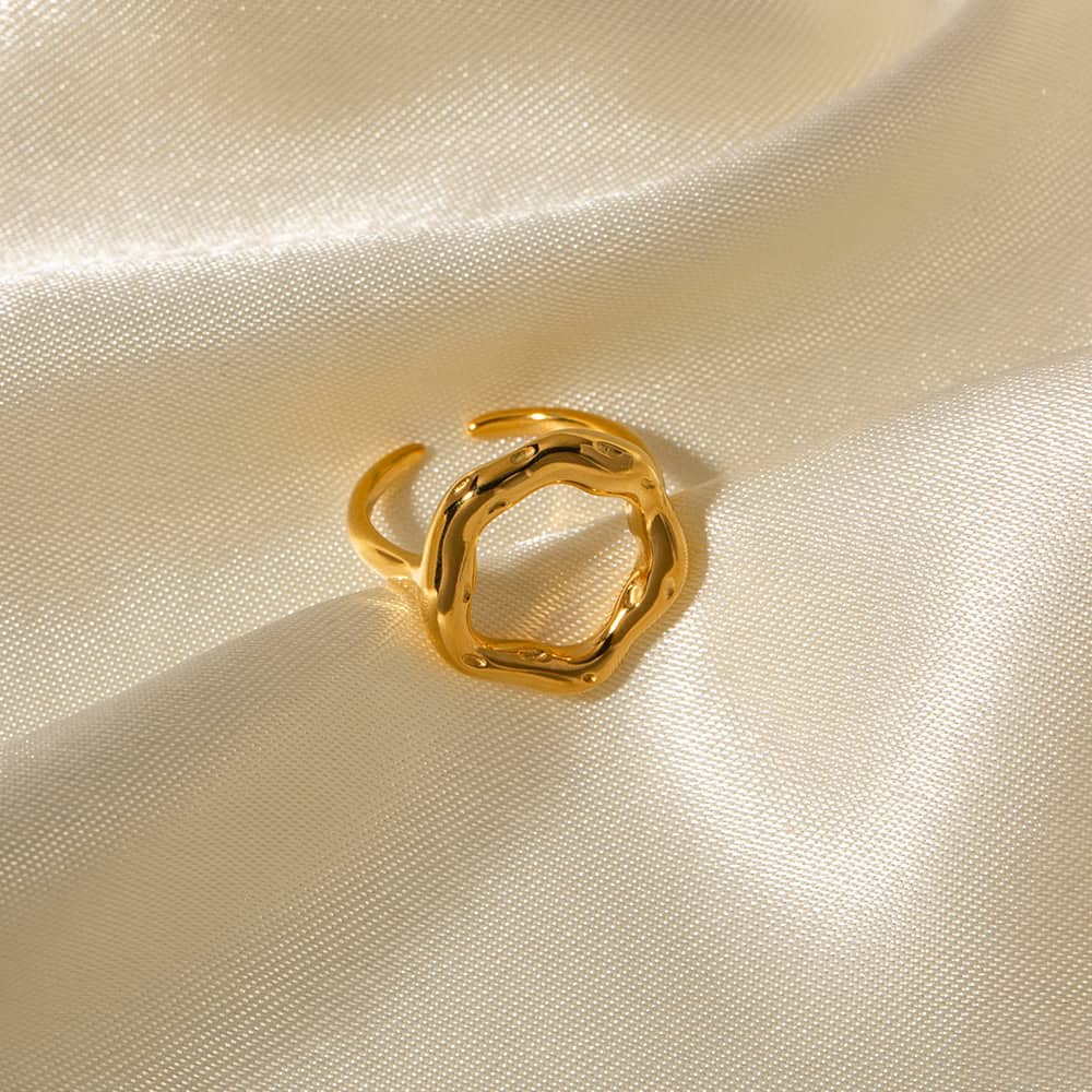 Alt text: Close-up of a stylish gold ring with an organic, irregular shape, placed on a silky, cream-colored fabric background, highlighting fine jewelry craftsmanship.