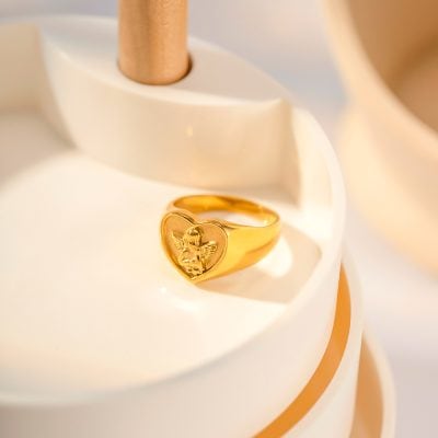 Close-up of a luxurious gold ring featuring a heart and angel charms, ideal for your jewelry collection. Perfect for special occasions, crafted with high-quality materials at Monalisa Medical Store.
