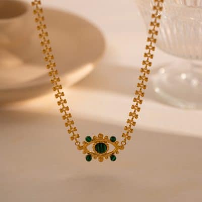 Close-up of a luxurious gold necklace featuring an eye-shaped pendant adorned with vibrant green beads, perfect for sophisticated jewelry lovers.