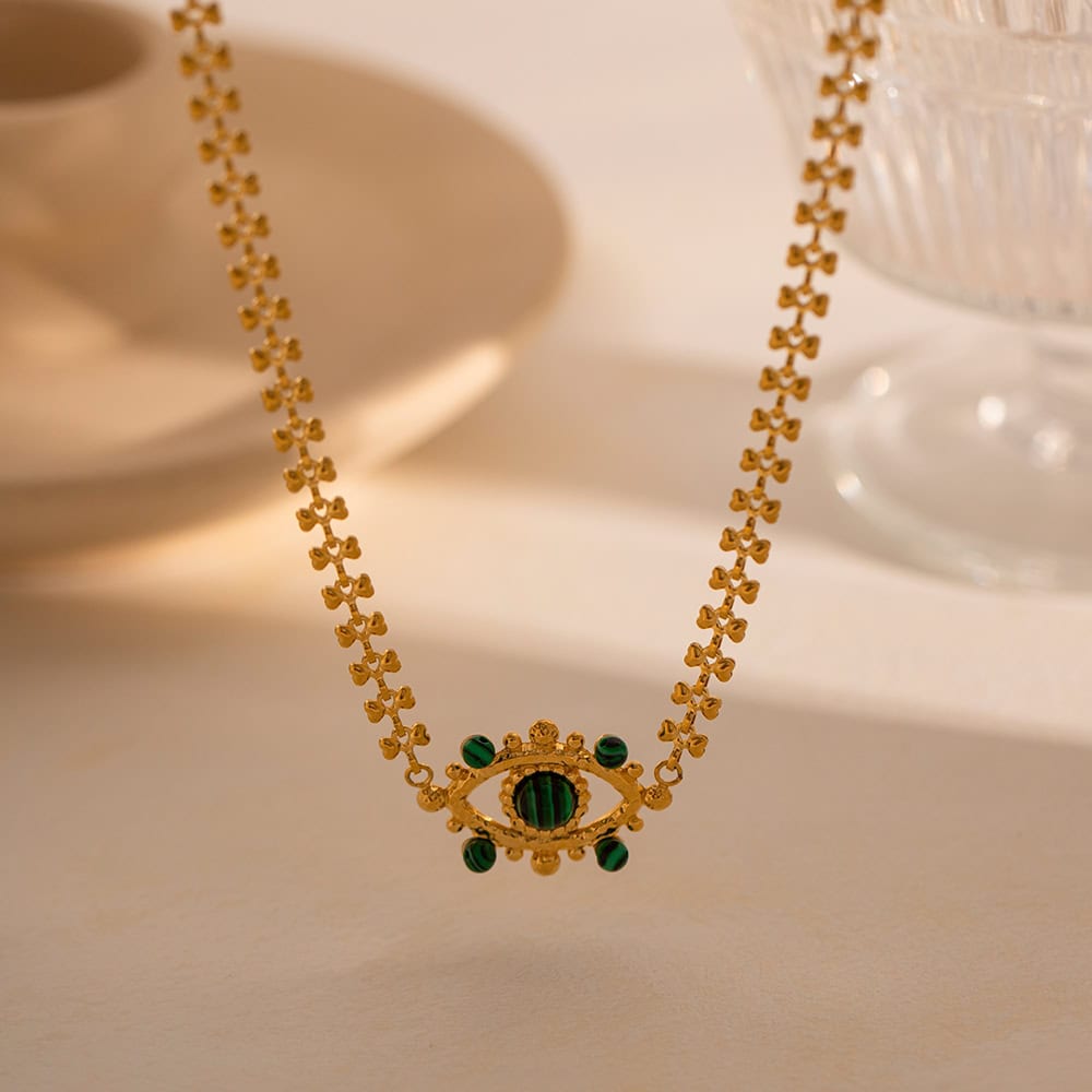 Close-up of a luxurious gold necklace featuring an eye-shaped pendant adorned with vibrant green beads, perfect for sophisticated jewelry lovers.