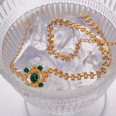 Luxurious gold necklace with green accent stones resting on ice cubes in a crystal bowl, showcasing fine jewelry craftsmanship for opt jewelry shoppers.