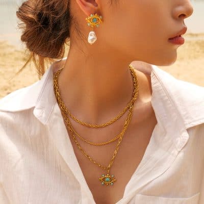 High-quality gold layered chain necklace with eye-shaped pendant, matching pearl earring, perfect for stylish women and jewelry lovers.