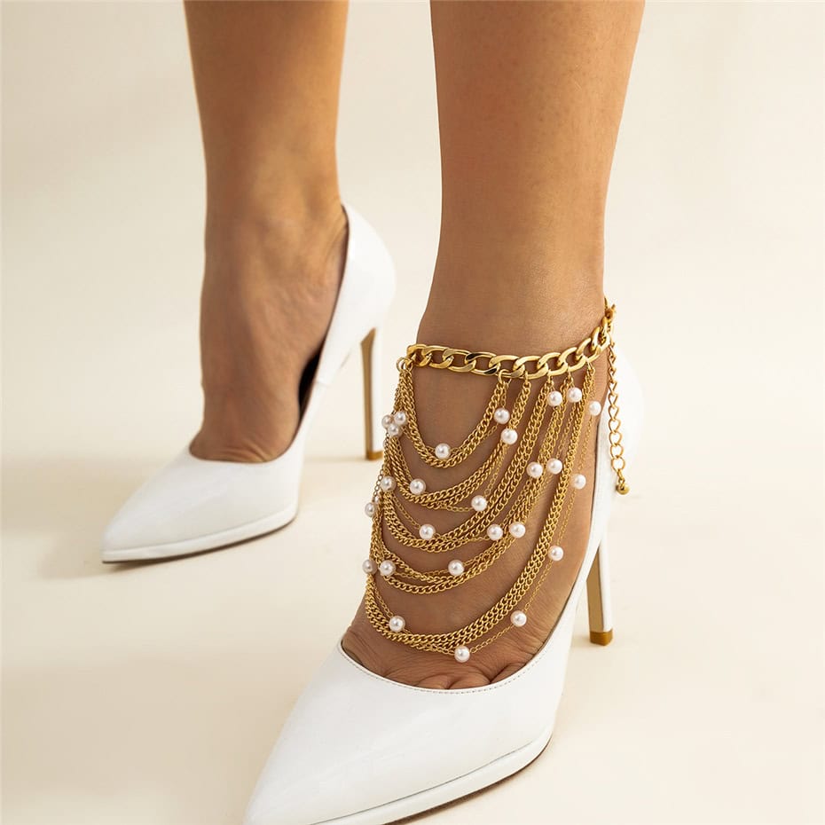 Stylish gold chain anklet with pearls, layered with chains on white stiletto heels, perfect for fashionable foot accessories and jewelry.