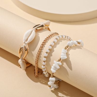 Beautiful seashell-inspired jewelry displayed on a cylindrical surface, featuring white shell beads and gold chains, perfect for beach and summer accessories.